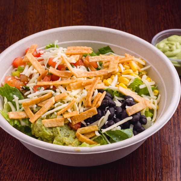 A vibrant salad bowl with lettuce, corn, black beans, guacamole, cheese, and tortilla strips.