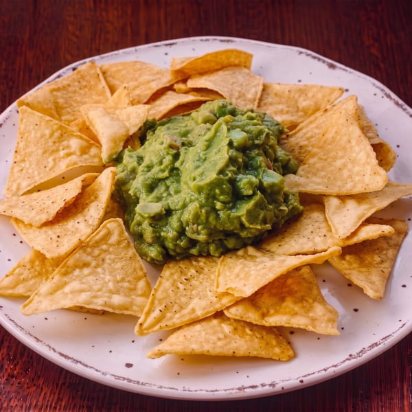 A white plate filled with golden tortilla chips surrounding a generous serving of green guacamole.