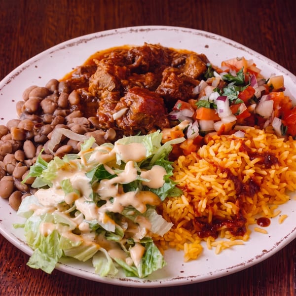 A plate of Mexican food with stewed meat, rice, beans, salsa, and a side salad.