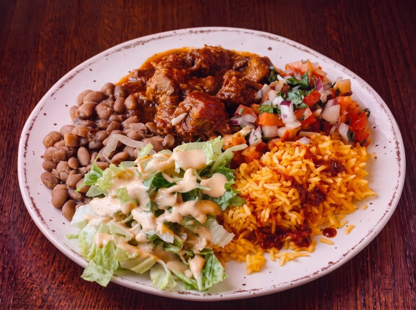 A plate of Mexican food with stewed meat, rice, beans, salsa, and a side salad.
