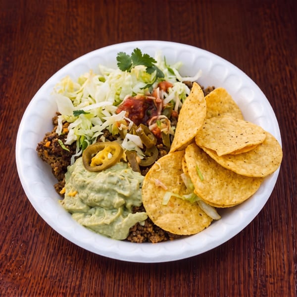 A white plate filled with ground meat, guacamole, salsa, shredded lettuce, jalapeños, and tortilla chips.
