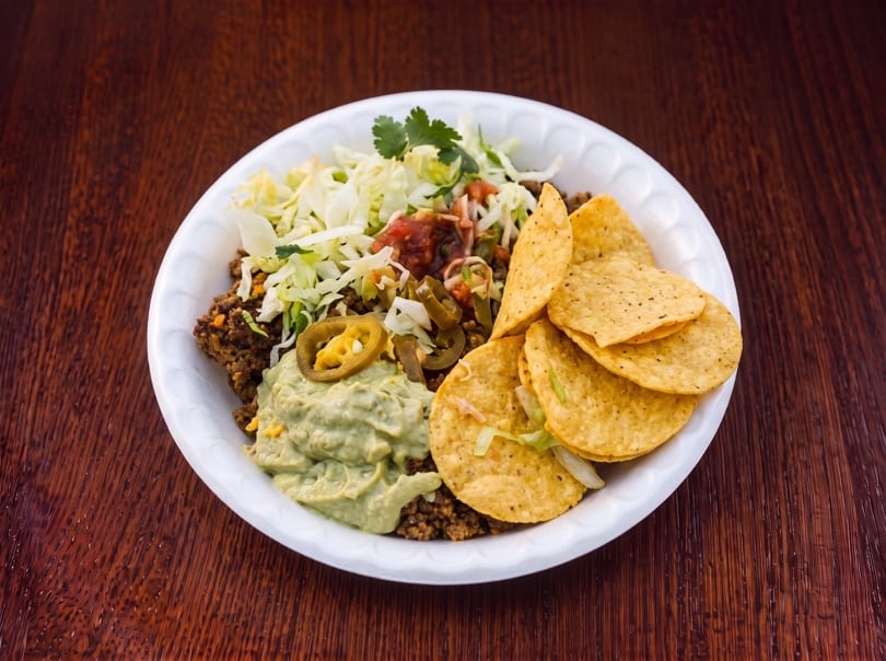 A white plate filled with ground meat, guacamole, salsa, shredded lettuce, jalapeños, and tortilla chips.