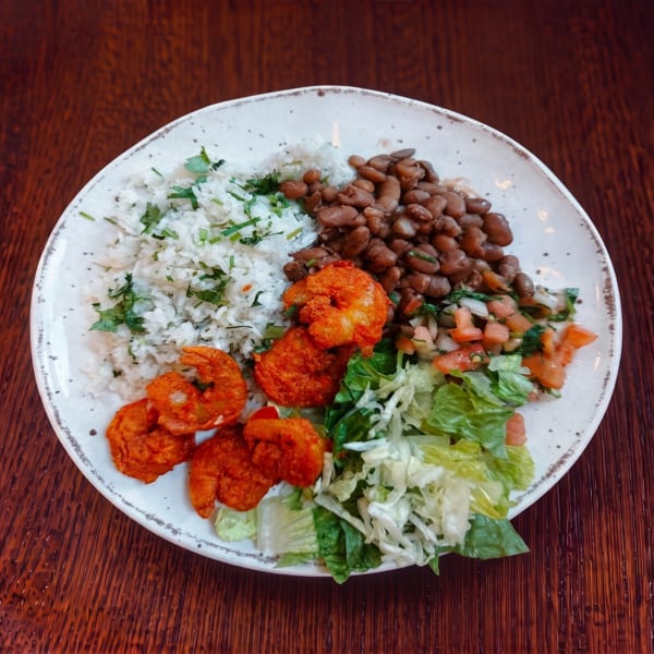A plate of fried shrimp, rice, beans, pico de gallo, and lettuce on a wooden table.