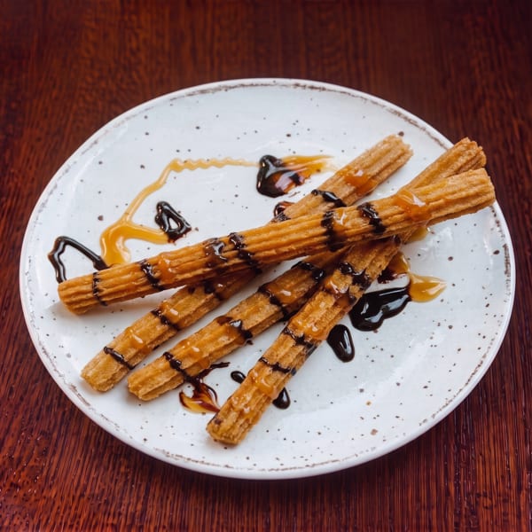 Churros drizzled with chocolate and caramel sauce on a white speckled plate.