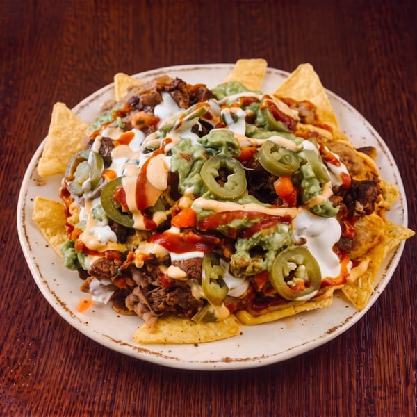 A large plate of loaded nachos with meat, guacamole, sour cream, salsa, and jalapeños.