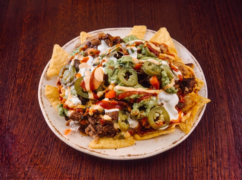 A large plate of loaded nachos with meat, guacamole, sour cream, salsa, and jalapeños.
