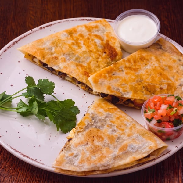 Three quesadilla slices with cilantro, sour cream, and pico de gallo on a white plate.