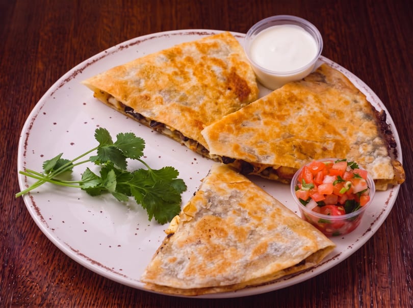 Three quesadilla slices with cilantro, sour cream, and pico de gallo on a white plate.