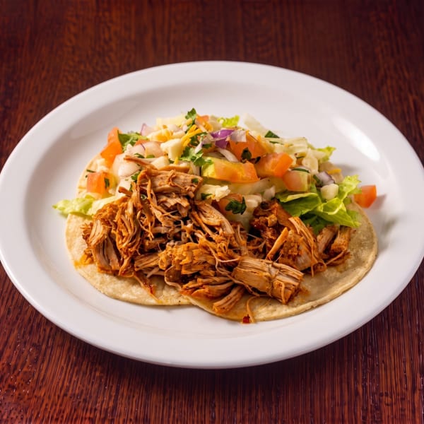 Shredded chicken taco with lettuce, tomatoes, and onions on a white plate.