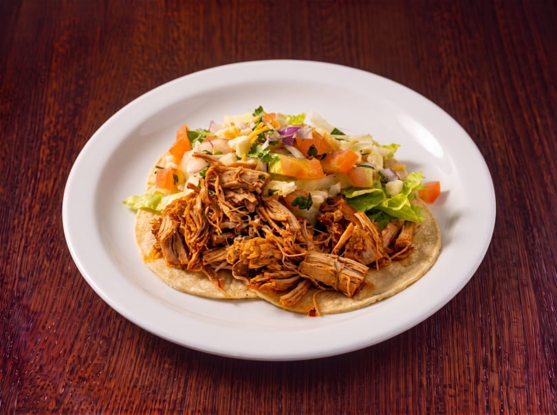 Shredded chicken taco with lettuce, tomatoes, and onions on a white plate.
